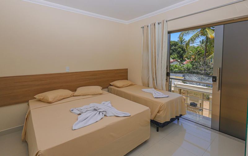 Quarto com cama de casal, cama de solteiro e porta para a varanda